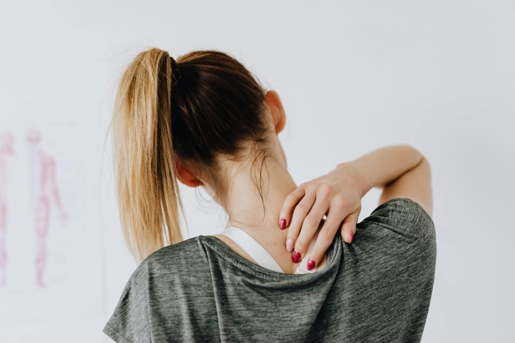 A woman in casual clothing holds her neck, indicating pain or discomfort.